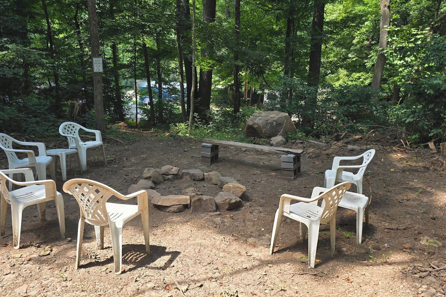 Un terrain de camping avec des chaises en plastique disposées autour d’un foyer, le tout entouré d’arbres.
