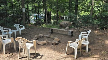 Un terrain de camping avec des chaises en plastique disposées autour d’un foyer, le tout entouré d’arbres.