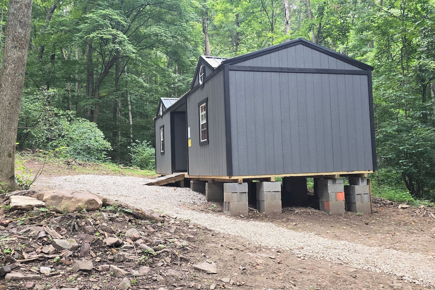 Two wooden cabins with a gravel path leading to them, surrounded by dense forest.