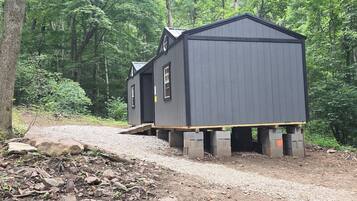 Two wooden cabins with a gravel path leading to them, surrounded by dense forest.