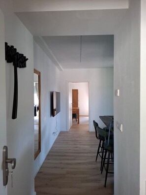 Un corridoio con pavimento in legno, una zona pranzo con sedie e tavolo, e uno specchio appeso al muro.