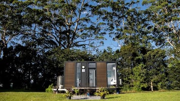 A modern, compact cabin with a flat roof, surrounded by lush greenery and trees.