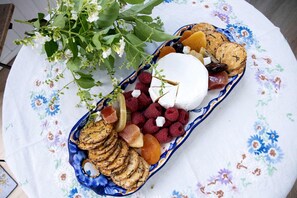 A table with a floral tablecloth, a blue and white plate with various snacks, and a branch of green leaves.