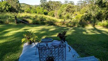 A grassy outdoor area with a metal table and chairs, surrounded by trees and a wooden fence.