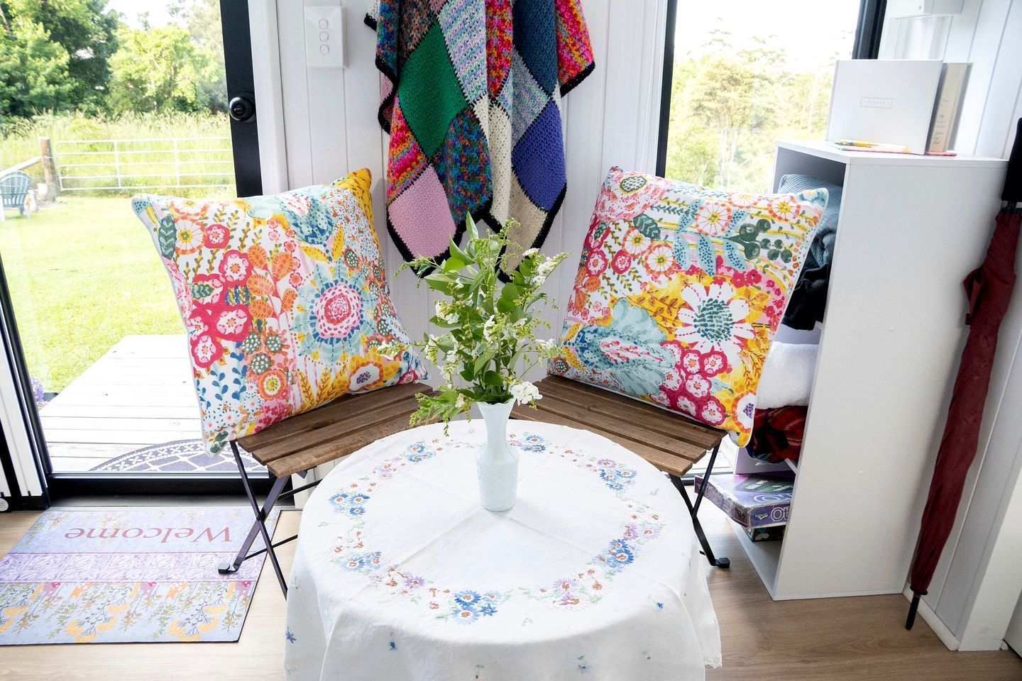A room with a bench, a small table with a vase, and colorful pillows.