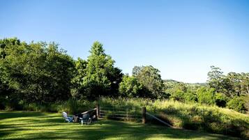 A grassy field with a wooden fence and a metal gate, surrounded by trees and hills.