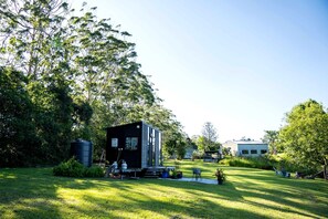 Uma casa moderna com uma pequena varanda, rodeada por um gramado bem cuidado e árvores.