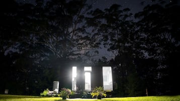 Une maison dotée de grandes fenêtres, entourée d’arbres et bordée d’une pelouse verdoyante.