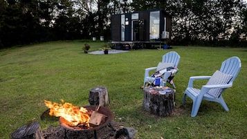 Un jardin avec un foyer, deux fauteuils Adirondack et un chalet moderne.