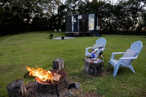 A backyard with a fire pit, two Adirondack chairs, and a modern cabin.