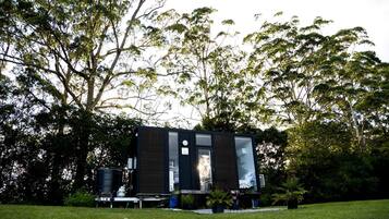 A modern, dark-colored building with a flat roof, surrounded by lush greenery and trees.
