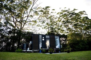A modern, dark-colored building with a flat roof, surrounded by lush greenery and trees.