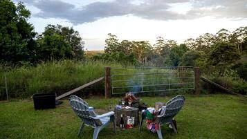 A grassy outdoor area with a metal gate, two chairs, a small table, and a fire pit.