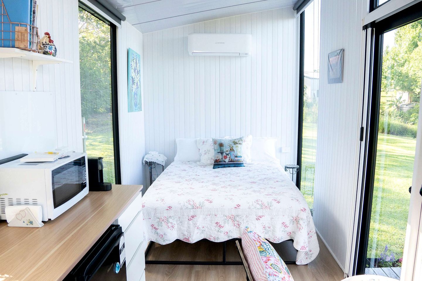 A bedroom with a bed, a desk with a microwave, and a view of the outdoors.