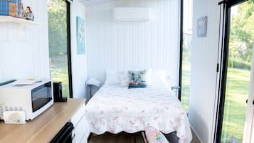 A bedroom with a bed, a desk with a microwave, and a view of the outdoors.