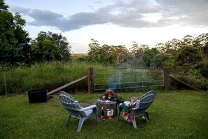 Área externa com gramado, portão de metal, duas cadeiras, uma pequena mesa e um braseiro.