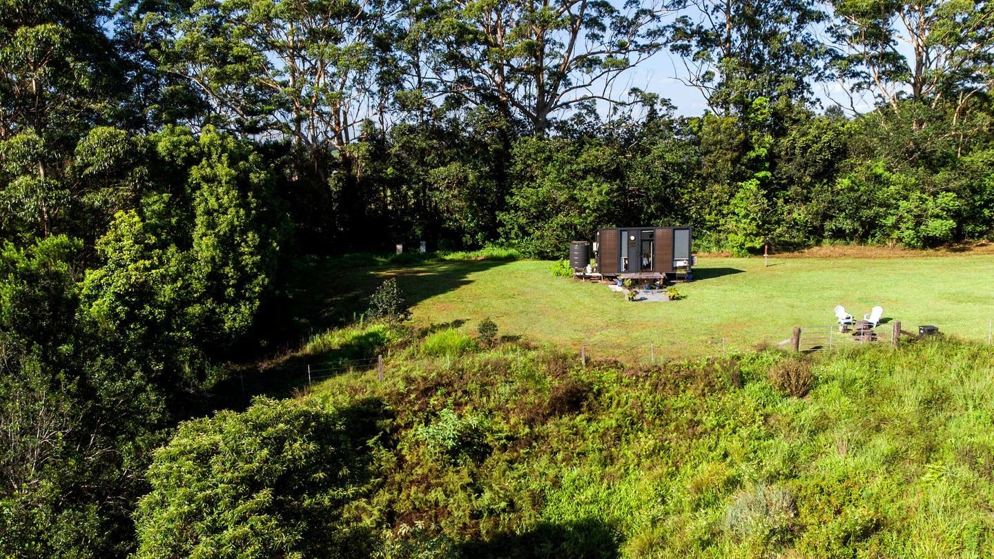 A small cabin with a single room, surrounded by a grassy area and dense trees.