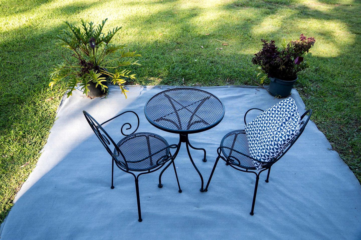 A patio with a round table and two chairs, surrounded by grass and potted plants.