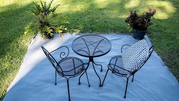 A patio with a round table and two chairs, surrounded by grass and potted plants.