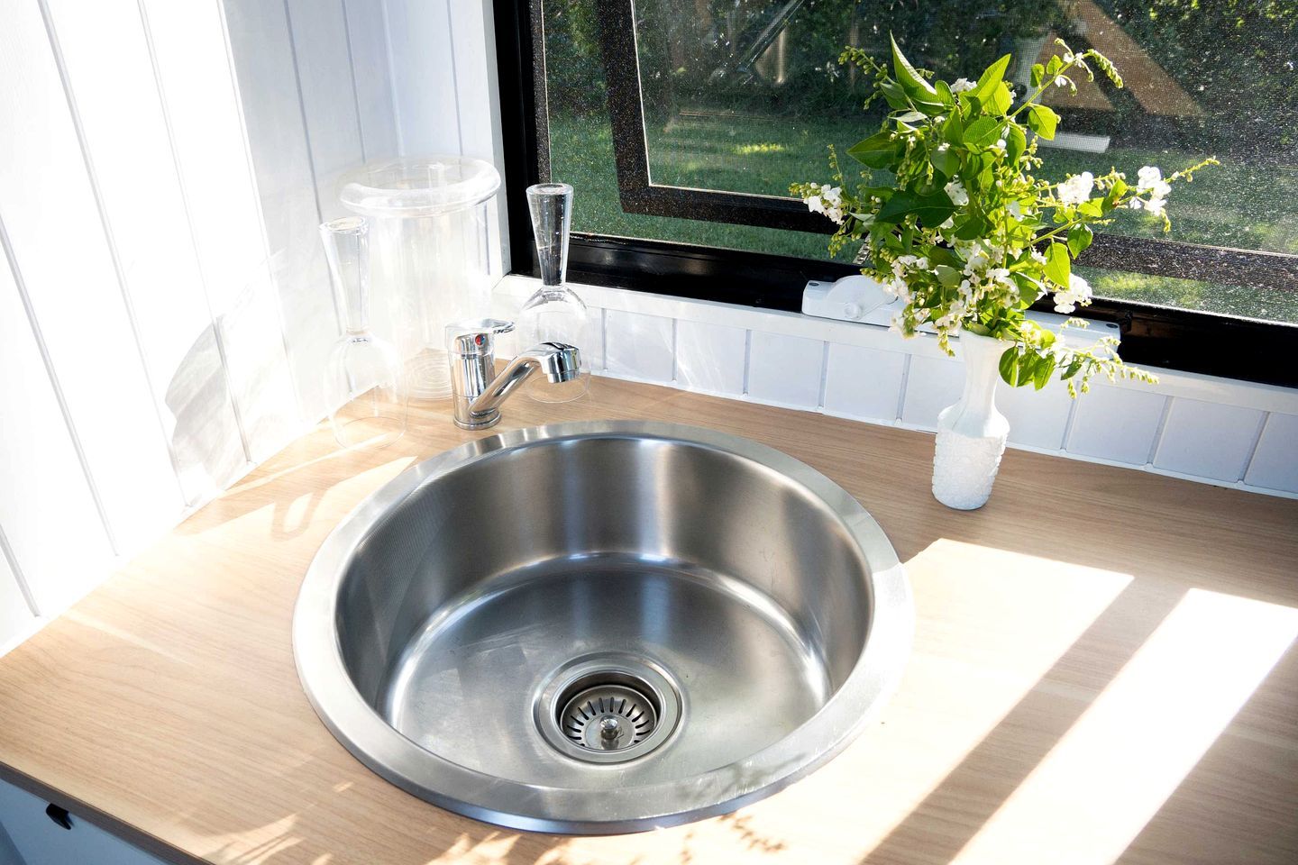 Ein Spülbecken aus Edelstahl mit einem modernen Wasserhahn, eine Topfpflanze und ein Fenster mit Blick auf Grünflächen.