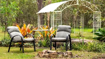 Two chairs with a table in a garden setting with a gazebo in the background.