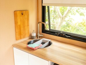 A kitchen with a sink, a cutting board, and a window with a view of trees. - Garden Glamping in a Queensland Tiny House for Relaxation and Recreation (Howard)