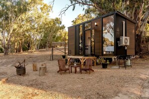 A small, modern cabin with a deck, surrounded by trees.