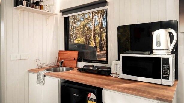 A compact kitchen with a wooden countertop, a microwave, a toaster, and a coffee maker. - Luminous Tiny House Perfect for Water and Winter Sports in Victoria, Australia (Howes Creek)