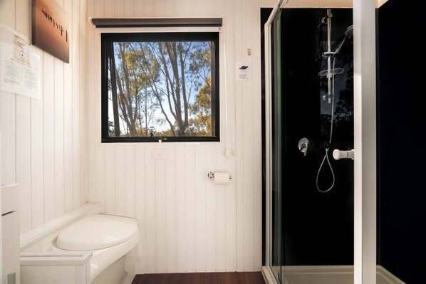 A bathroom with a toilet, a window with a view of trees, and a shower with a glass door.