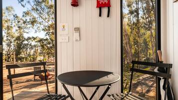 A room with a table and two chairs, a fire extinguisher, a blanket, and a window with a view of trees.