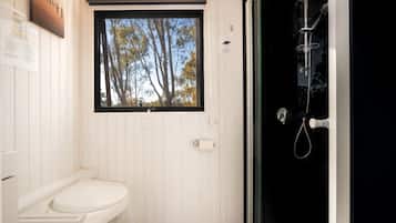 Een badkamer met toilet, een raam met uitzicht op bomen en een douche met een glazen deur.