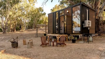 Een kleine, moderne cabin met een terras, omringd door bomen.