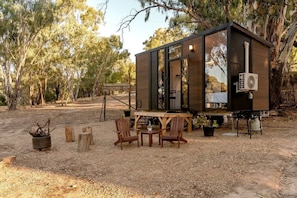 A small, modern cabin with a deck, surrounded by trees.