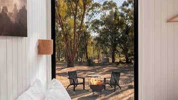 A bedroom with a bed, a view of an outdoor area with a fire pit and chairs, and a painting on the wall.