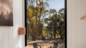 A bedroom with a bed, a view of an outdoor area with a fire pit and chairs, and a painting on the wall. - Luminous Tiny House Perfect for Water and Winter Sports in Victoria, Australia (Howes Creek)