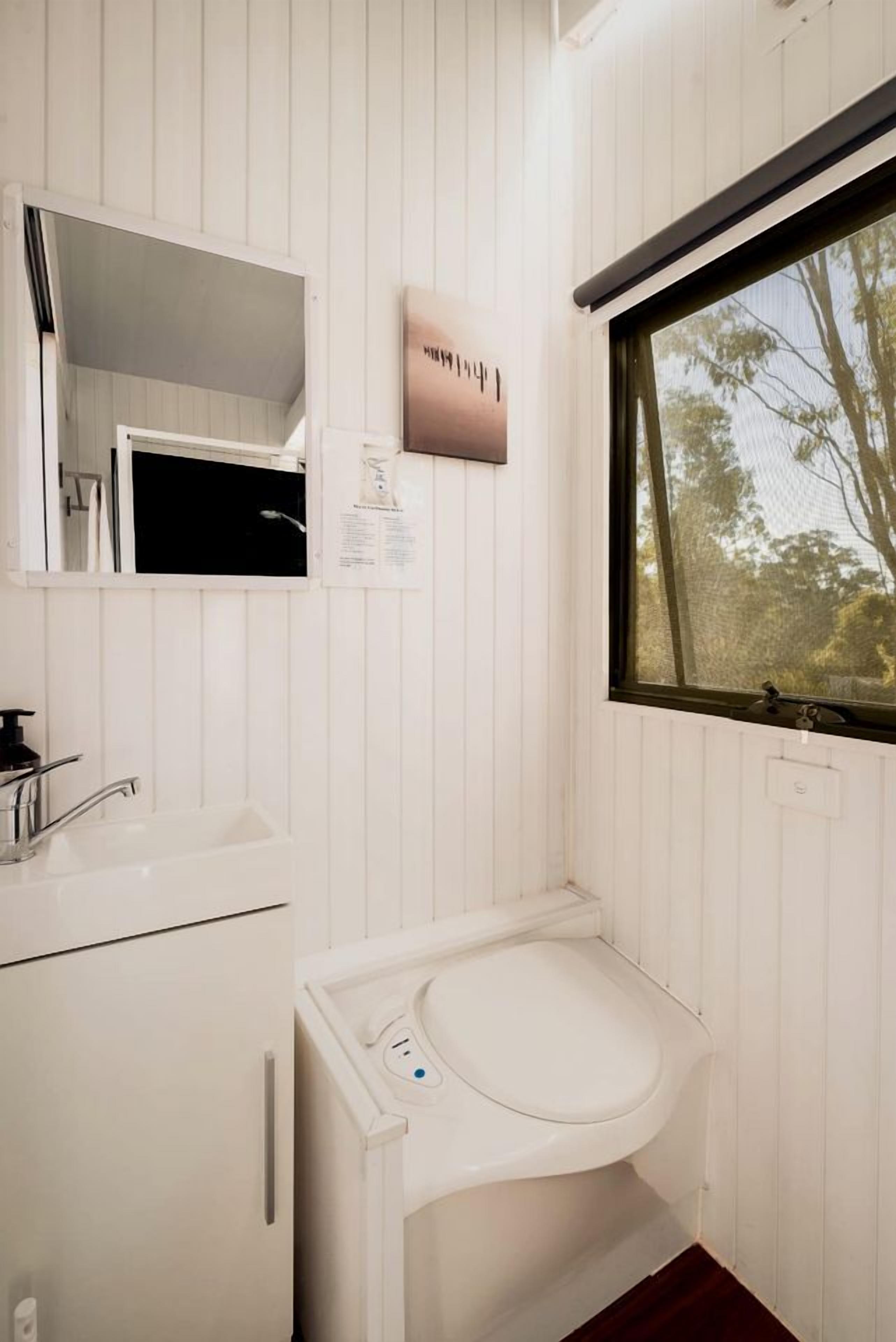 A bathroom with a white sink, a mirror, a window, and a toilet.