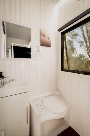 A bathroom with a white sink, a mirror, a window, and a toilet.