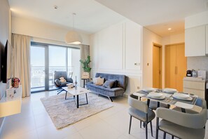 A modern living room with a sofa, a dining table set for four, and a large window with curtains. - Rentico Lux 1BR Skyline View Burj Royale (Dubai)