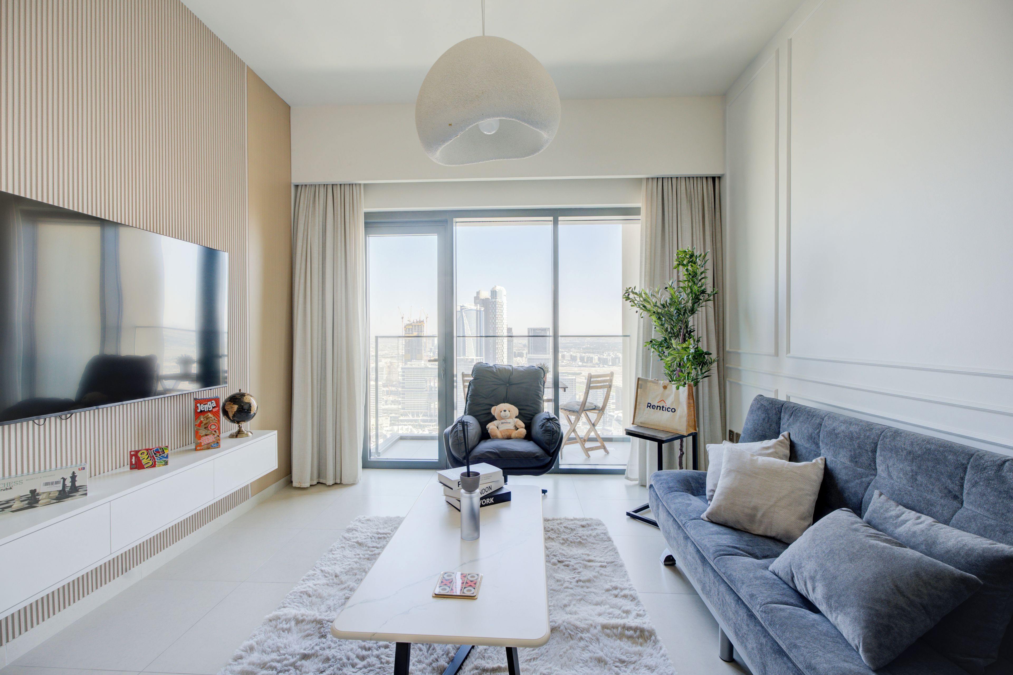 A modern living room with a flat-screen TV, a sofa, a coffee table, and a view of the city through large windows.