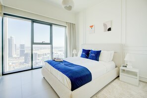 A modern bedroom with a large bed, a nightstand, a lamp, and a view of a cityscape through floor-to-ceiling windows. - Rentico Lux 1BR Skyline View Burj Royale (Dubai)