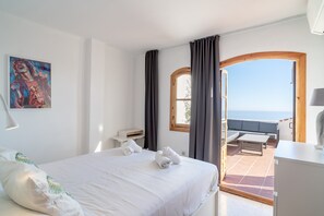 Ein Hotelzimmer mit Bett, Schreibtisch, einem Fenster mit Vorhängen und Blick aufs Meer.