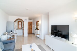 Ein modernes Wohnzimmer mit Flachbildfernseher, einer Couch, einem Couchtisch und einer Küche im Hintergrund.