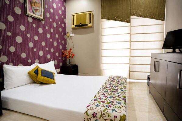 A hotel room with a bed, a dresser, a window with blinds, and a wall with a polka dot pattern.
