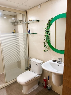 Un baño moderno con cabina de ducha de vidrio, inodoro, lavamanos y espejo con marco verde.