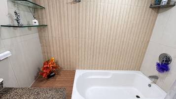 Un baño con una bañera, un estante de vidrio con artículos de aseo y una planta decorativa.