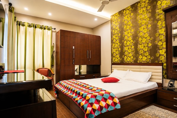 A hotel room with a bed, a desk, a chair, a wardrobe, and a mirror. - Elegant 3BR Apartment in Mohali (Sahibzada Ajit Singh Nagar)