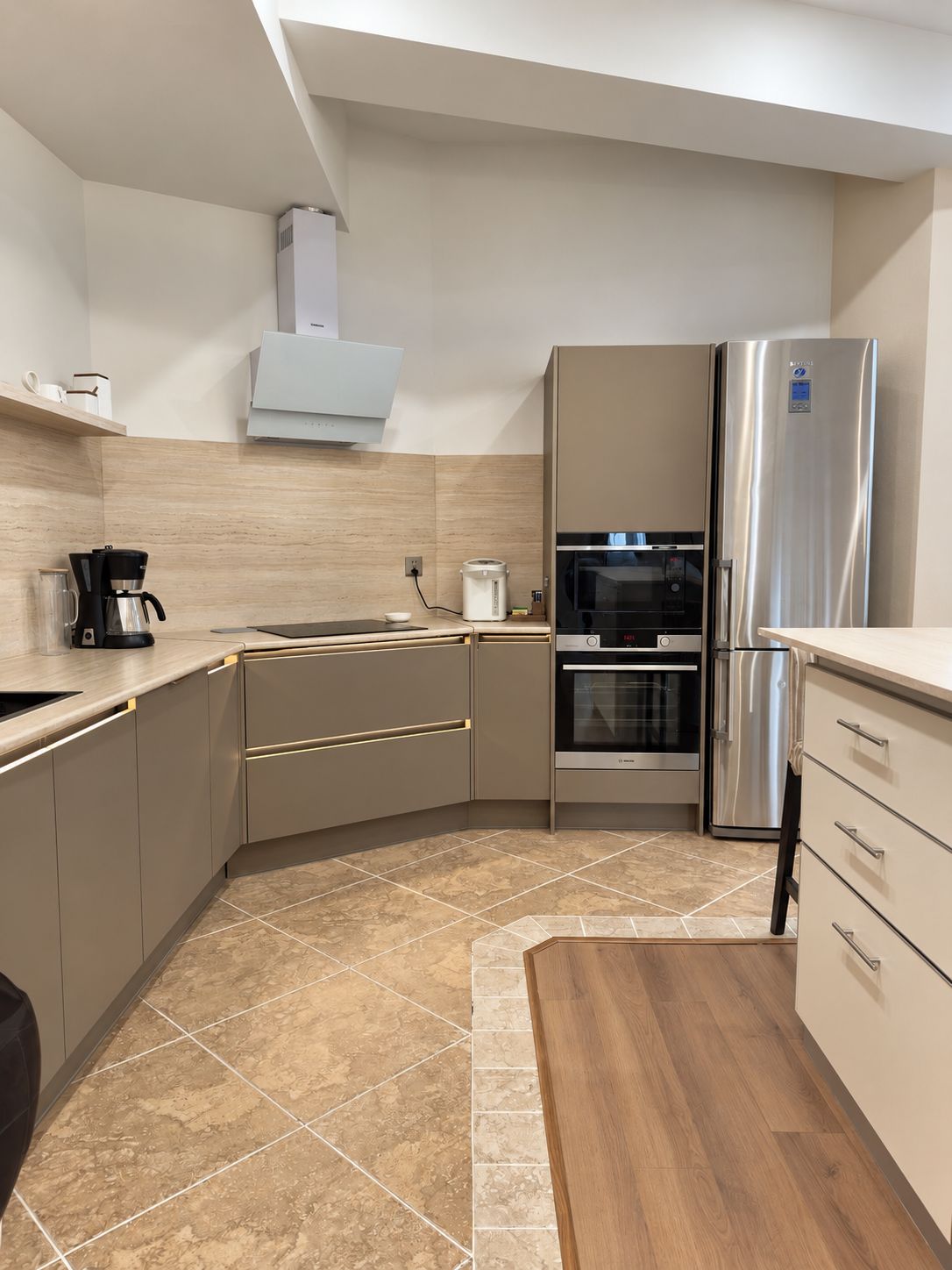 A modern kitchen with a built-in oven, a stainless steel refrigerator, and a coffee maker.