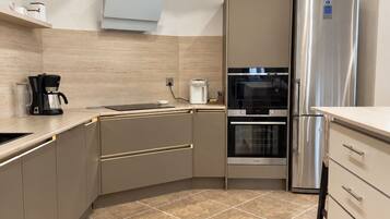 A modern kitchen with a built-in oven, a stainless steel refrigerator, and a coffee maker.