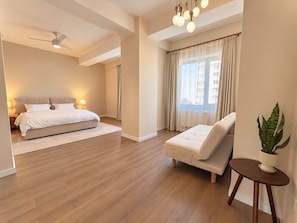 Een moderne slaapkamer met een groot bed, een zithoek met een fauteuil, een klein tafeltje en een pot met een plant.