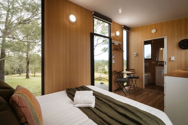 Un dormitorio moderno con una cama grande, piso de madera, un comedor y vistas al exterior.